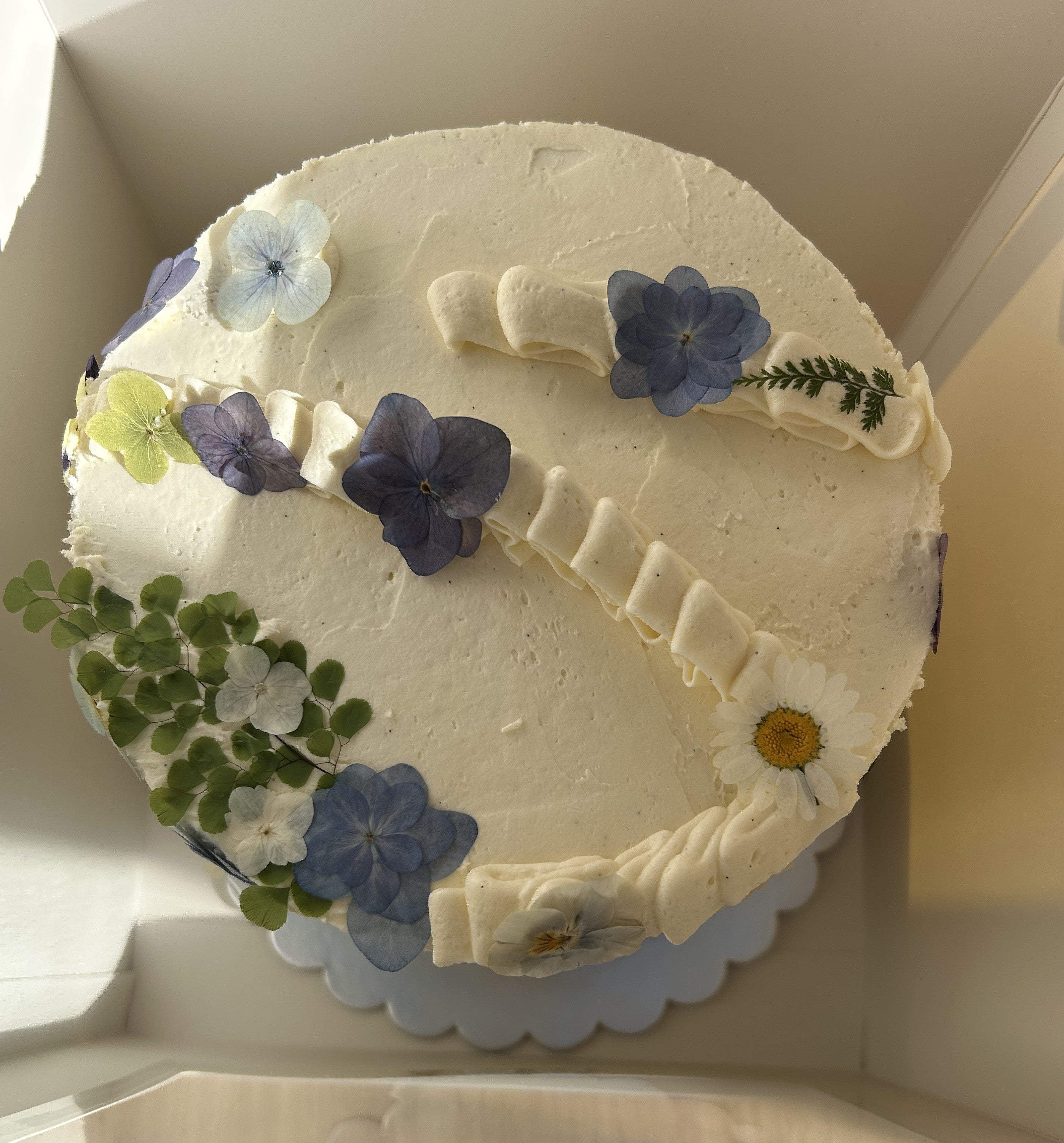 Round cake with white frosting and floral decorations in a box.