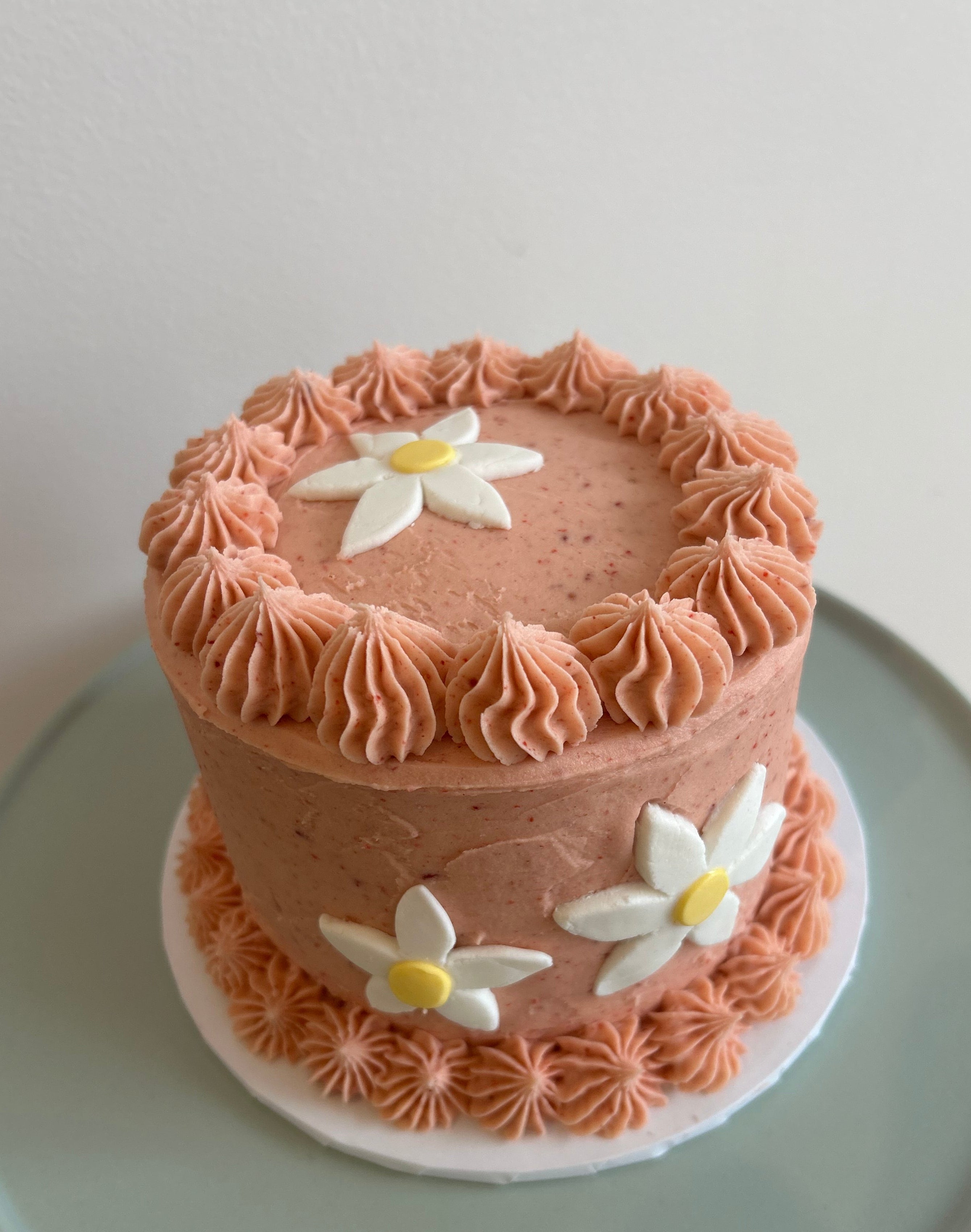 Small round cake with strawberry frosting and white flowers on a light green plate.